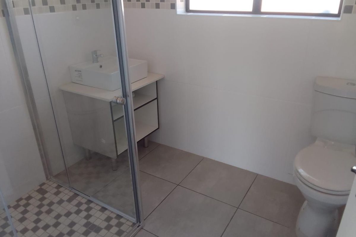 A clean, modern bathroom featuring a glass-enclosed shower, a contemporary vanity with a basin, and a standard toilet with neutral floor and wall tiling.
