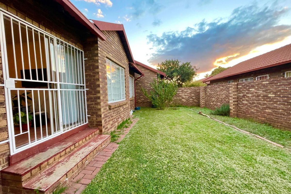A private rear garden featuring a brick-paved patio area, established lawn, and perimeter brick walling, accessible via sliding doors with security gates.