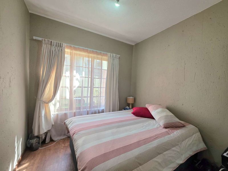 A standard bedroom featuring textured walls, laminated flooring, and a window with a grid pattern, providing natural light.