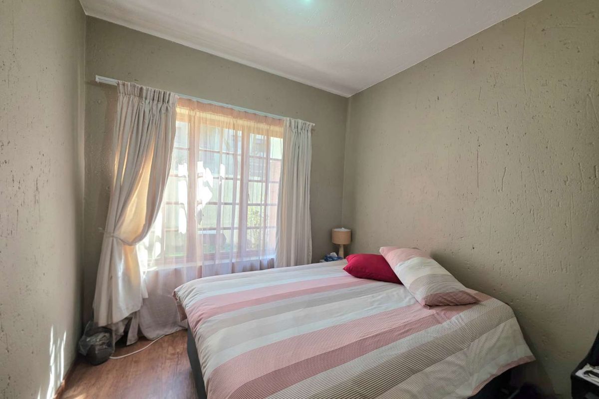 A standard bedroom featuring textured walls, laminated flooring, and a window with a grid pattern, providing natural light.