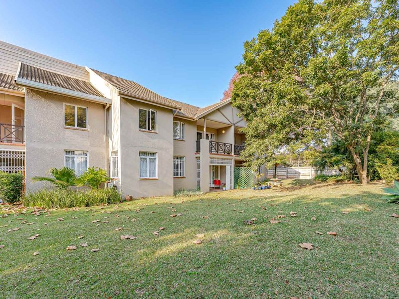 Rear view of the apartment building featuring a well-maintained lawn, mature trees, and private balconies with security gates.