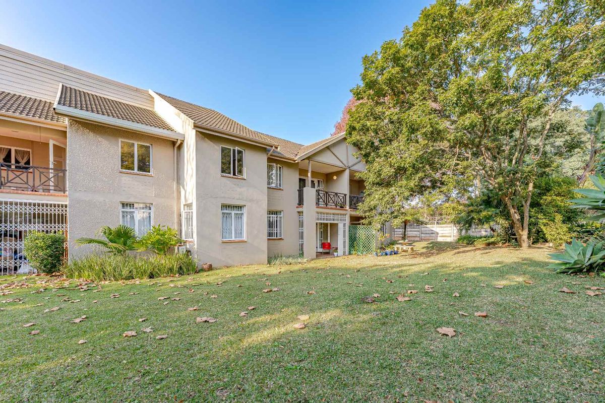 Rear view of the apartment building featuring a well-maintained lawn, mature trees, and private balconies with security gates.