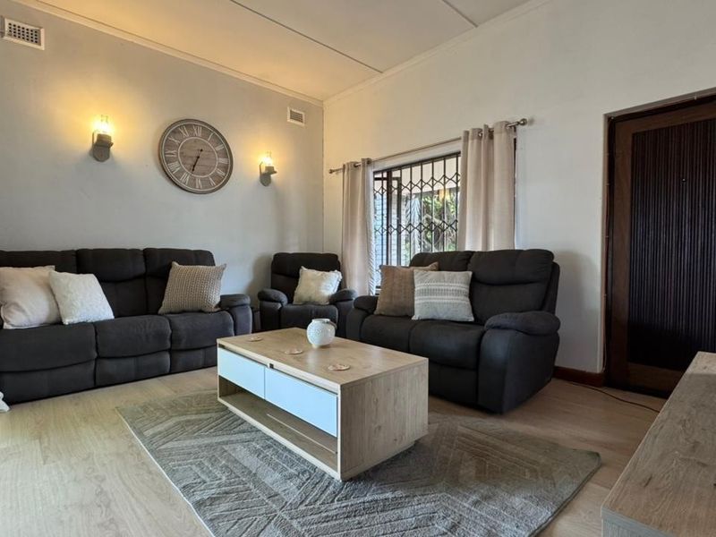 A comfortable living room featuring light laminate flooring, wall-mounted lighting, and a secure entrance door with a security gate.