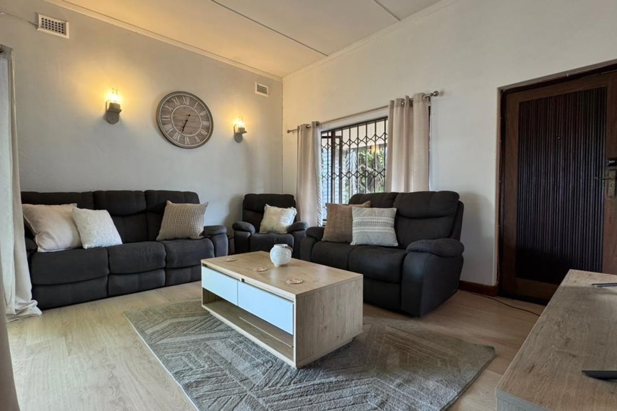 A comfortable living room featuring light laminate flooring, wall-mounted lighting, and a secure entrance door with a security gate.