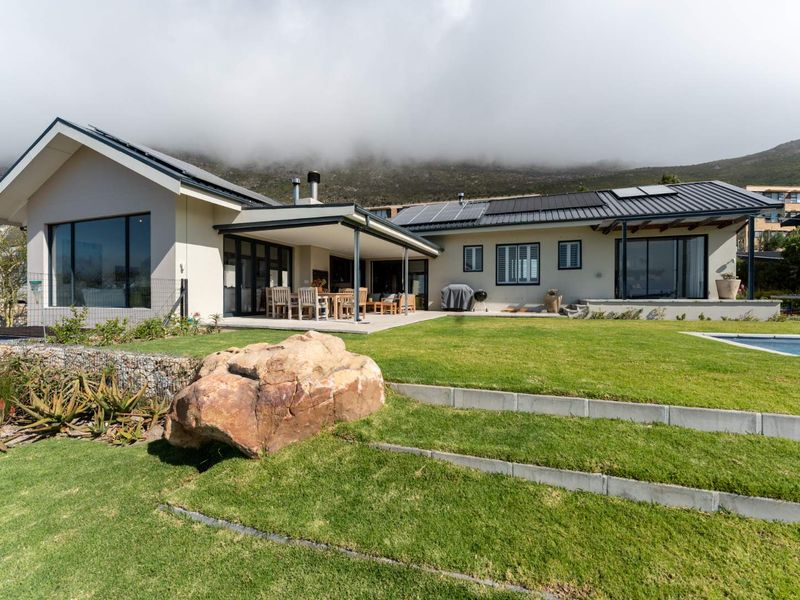 Rear view of a modern home featuring a covered patio, swimming pool, landscaped garden, and solar panels set against a mountain backdrop.