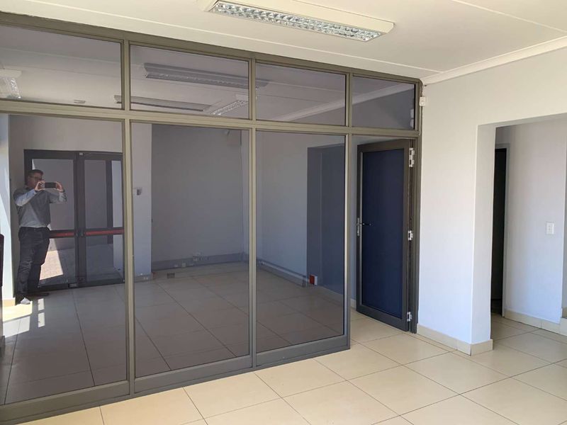 A clean, vacant office space featuring modern aluminium-framed glass partitioning, tiled flooring, and recessed fluorescent lighting, suitable for professional use.