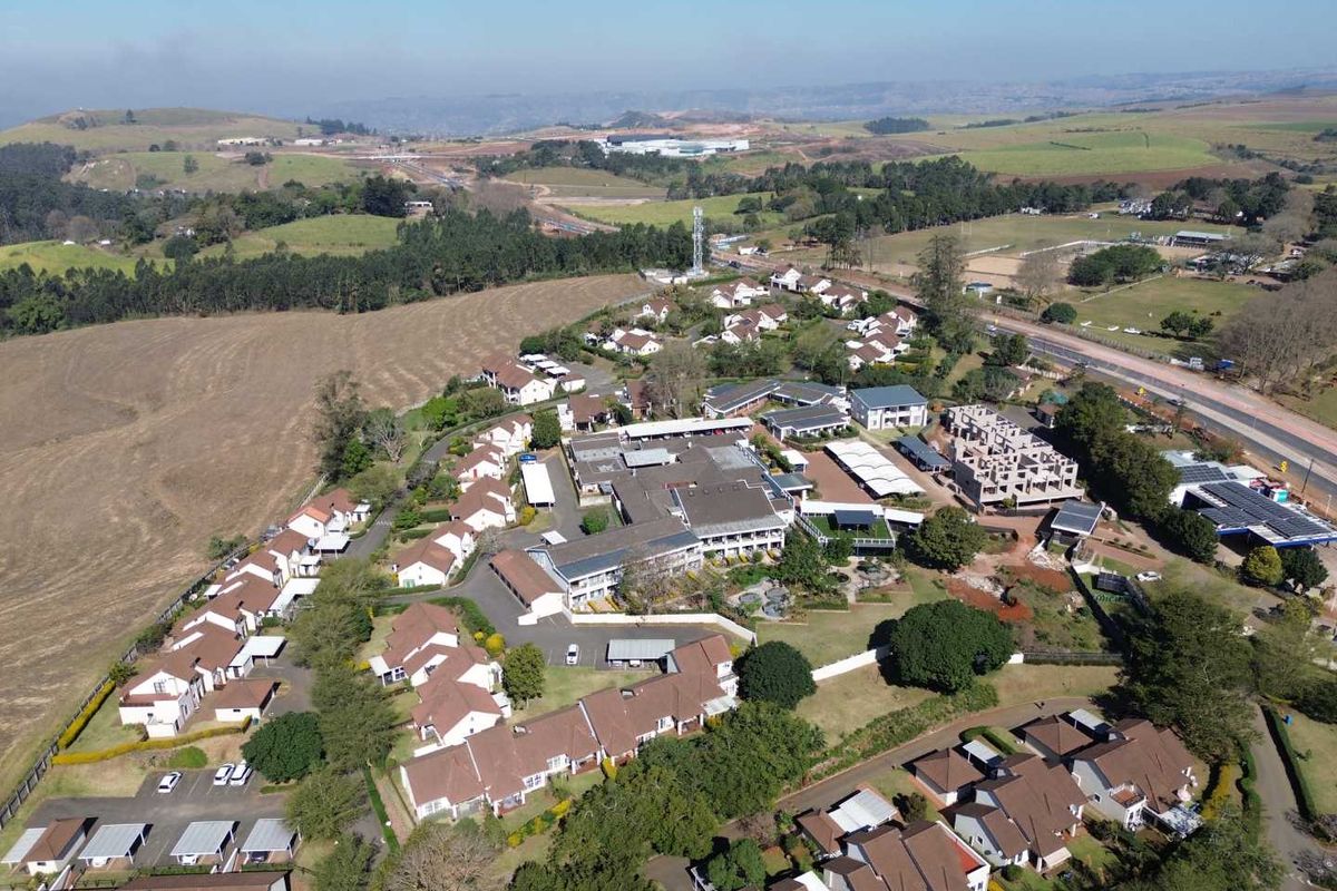 An aerial view of a residential townhouse complex situated in a rural landscape, featuring multiple units, paved driveways, and surrounding green space.