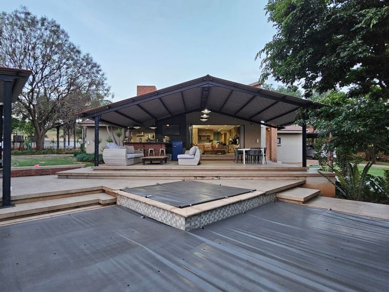Spacious covered patio featuring a built-in braai area, overlooking a swimming pool with a deck, perfect for outdoor entertaining.