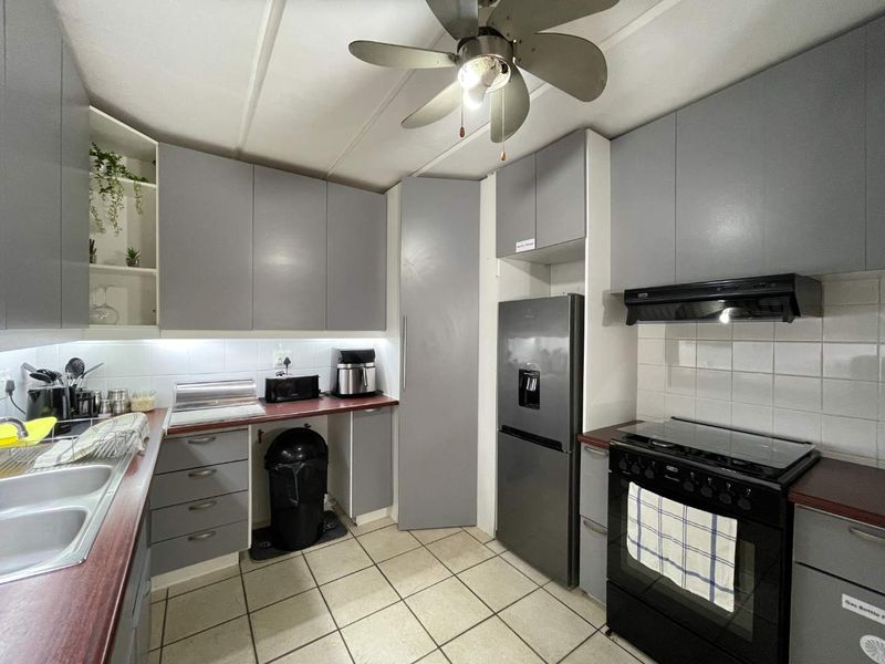 A functional kitchen featuring grey cabinetry, laminate countertops, a tiled backsplash, and a freestanding stove with an extractor fan.