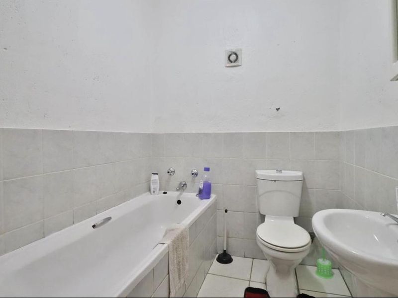 A functional bathroom featuring a standard bathtub, pedestal basin, and toilet with tiled finishes and a wall-mounted extractor fan.