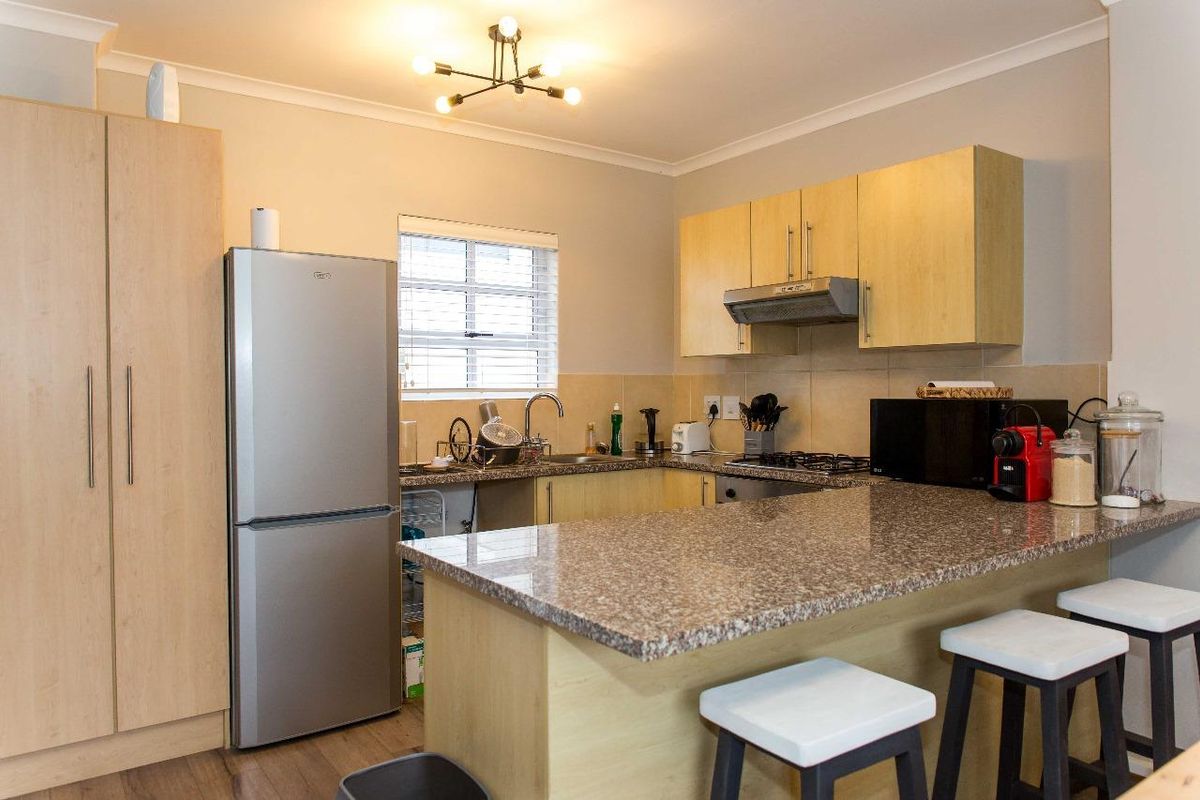 A functional kitchen featuring light wood-look cabinetry, granite countertops, a breakfast bar, and integrated appliances including a gas hob and extractor fan.