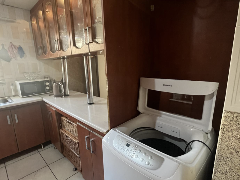 A functional laundry area featuring built-in wooden cabinetry, laminate countertops, a stainless steel sink, and tiled flooring.