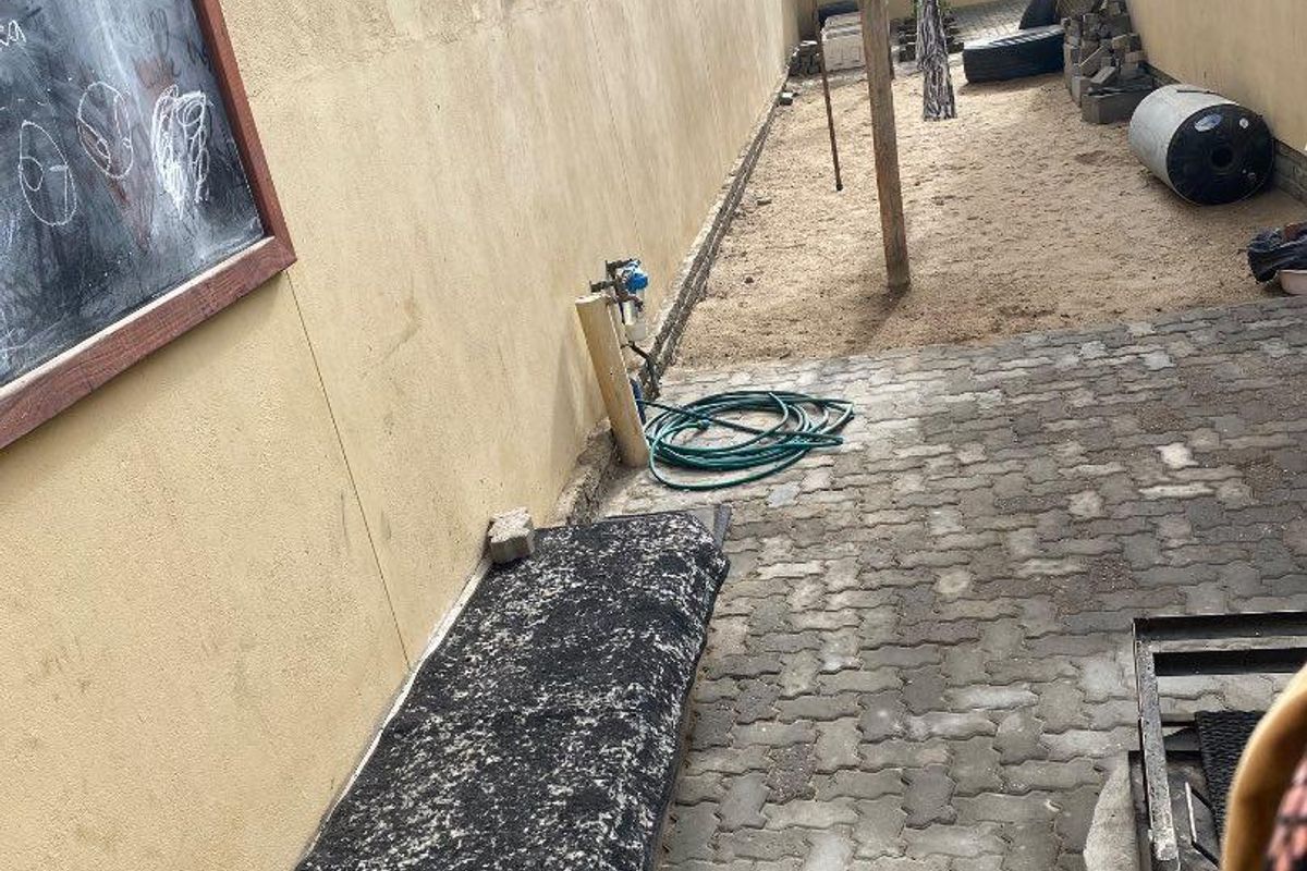A side exterior area featuring paved flooring, a concrete boundary wall, and a utility space with a water connection point.