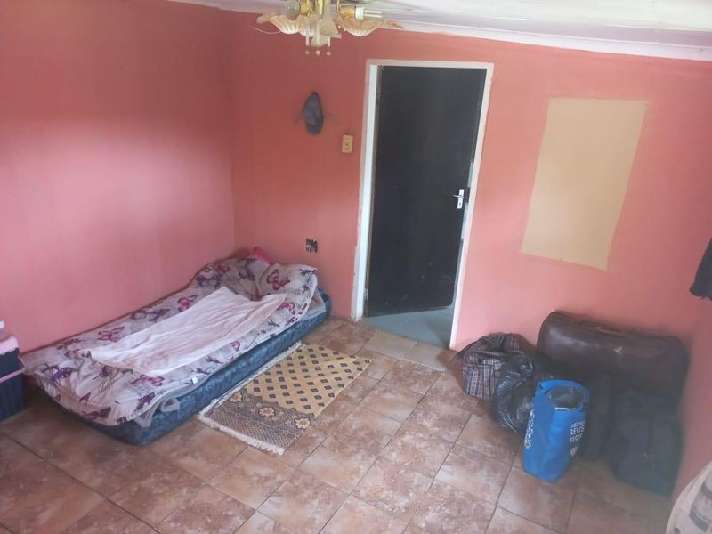 A bedroom featuring tiled flooring and a ceiling light fixture, currently requiring cosmetic updates and wall repairs.