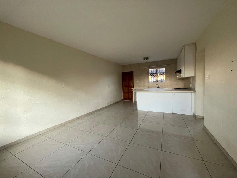 An open-plan living and kitchen area featuring tiled flooring, basic cabinetry, and a built-in hob with extractor fan.