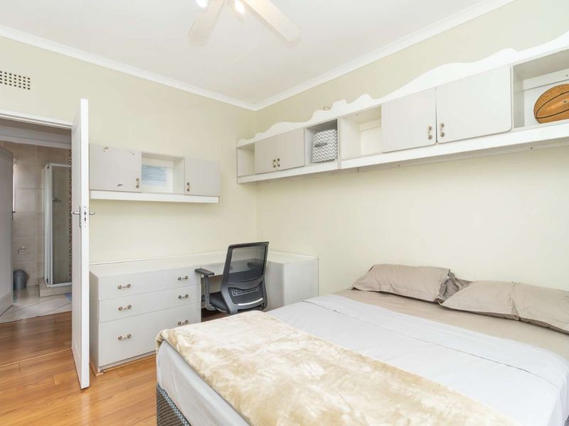 Bedroom featuring built-in cabinetry, a desk area, ceiling fan, and laminate flooring, with direct access to an en-suite bathroom.