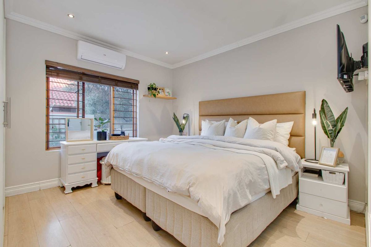 A well-maintained bedroom featuring light wood-look flooring, crown molding, and a wall-mounted air conditioning unit.
