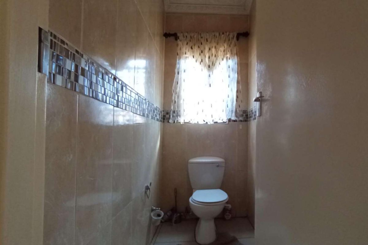 A compact bathroom featuring floor-to-ceiling wall tiles with a decorative mosaic border and a standard white toilet suite.