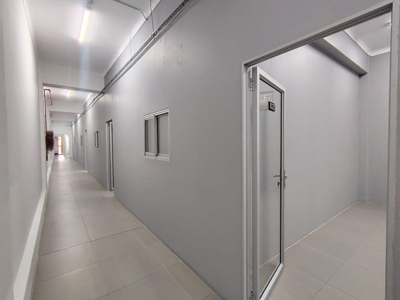 A clean, modern office hallway featuring tiled flooring, neutral grey walls, and multiple access points with aluminium-framed doors.