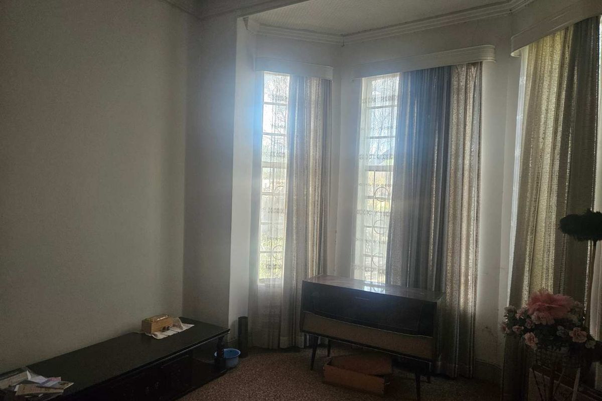 A living room featuring a large bay window with natural light, original crown molding, and carpeted flooring.