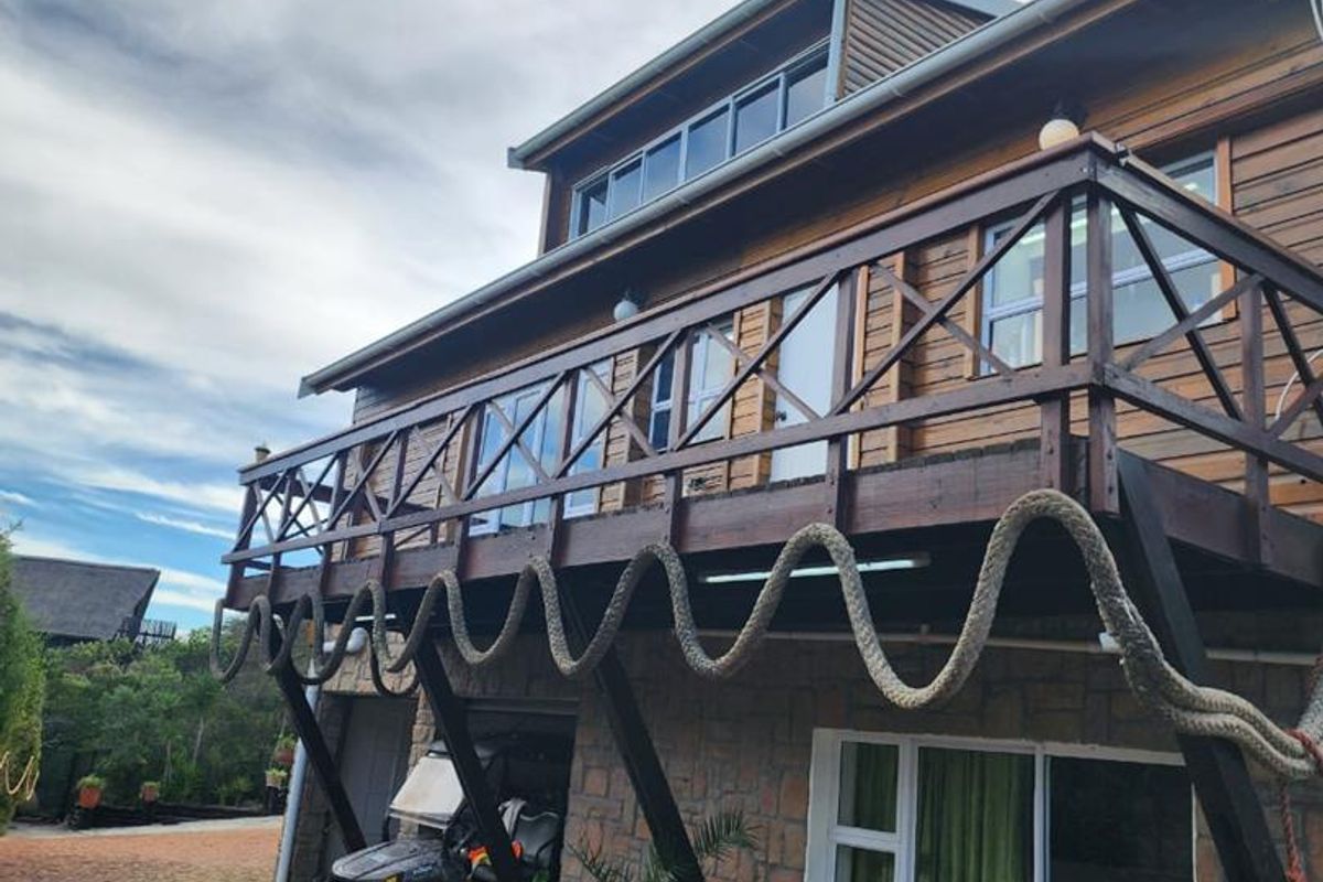 Rear elevation of a multi-story home featuring a timber balcony, stone cladding, and sliding glass doors opening onto a paved driveway area.
