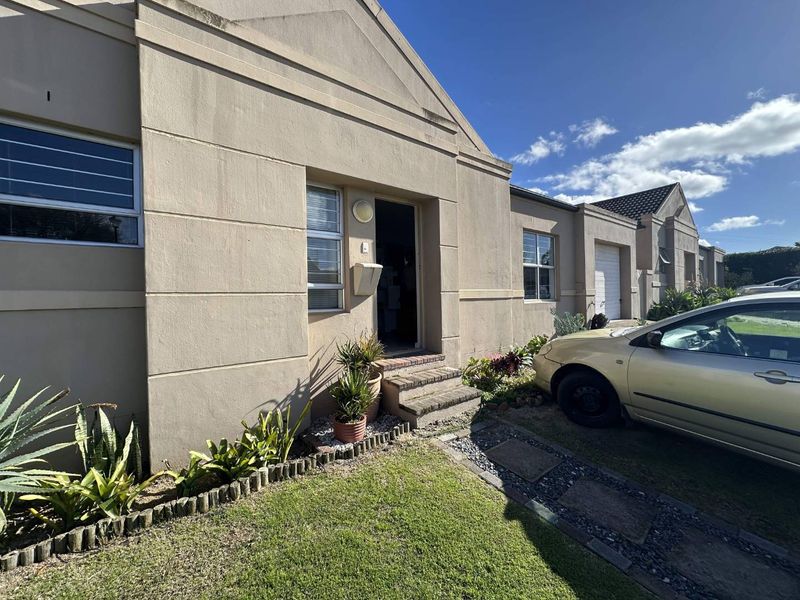 Front elevation of a townhouse featuring a plastered facade, brick entrance steps, and a paved walkway leading to the main entrance.