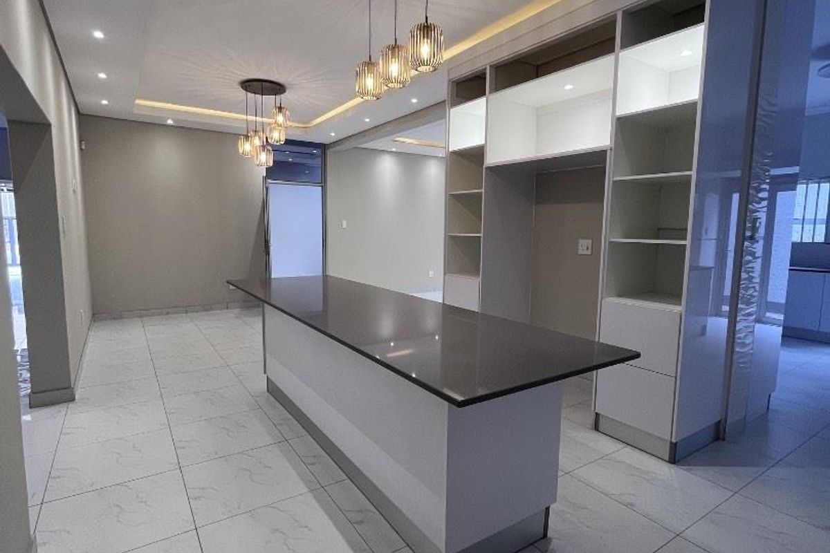 Modern, spacious kitchen featuring a large central island with stone countertops, sleek built-in cabinetry, and elegant recessed and pendant lighting throughout.