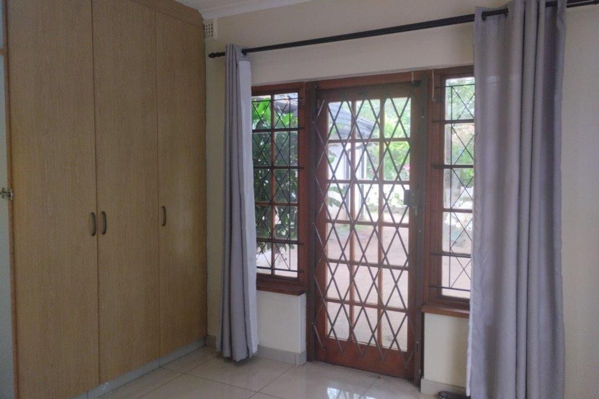 A bright bedroom featuring built-in wooden cupboards, tiled flooring, and a secure wooden door with access to the exterior.