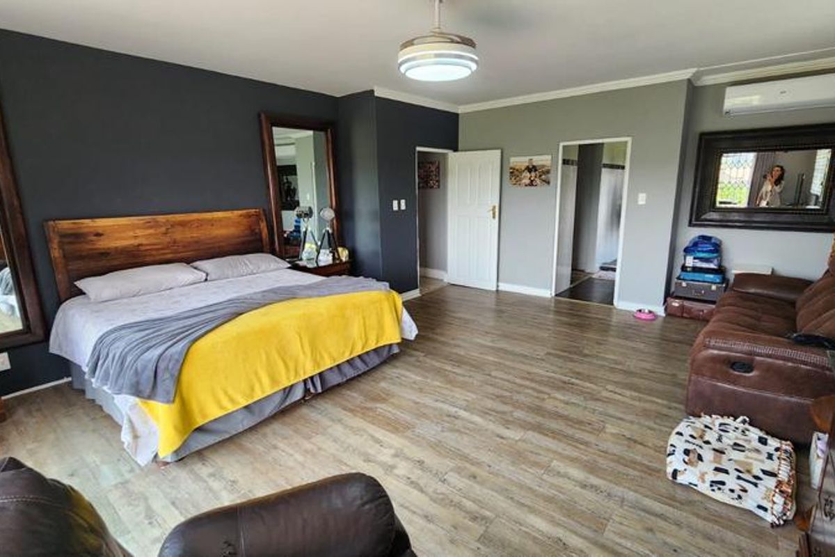 Spacious bedroom featuring wood-look flooring, a split-system air conditioning unit, and direct access to an adjoining room.