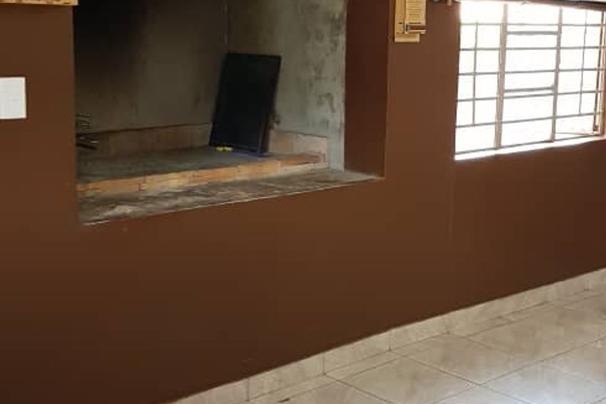 Indoor entertainment area featuring a built-in brick braai fireplace, tiled flooring, and window blinds.