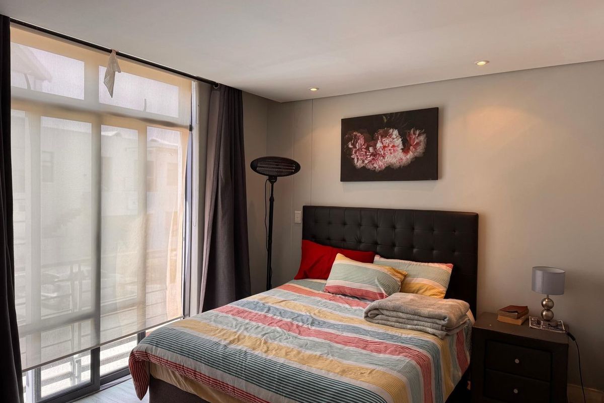 A well-lit bedroom featuring floor-to-ceiling sliding glass doors that provide access to a balcony and allow for ample natural light.
