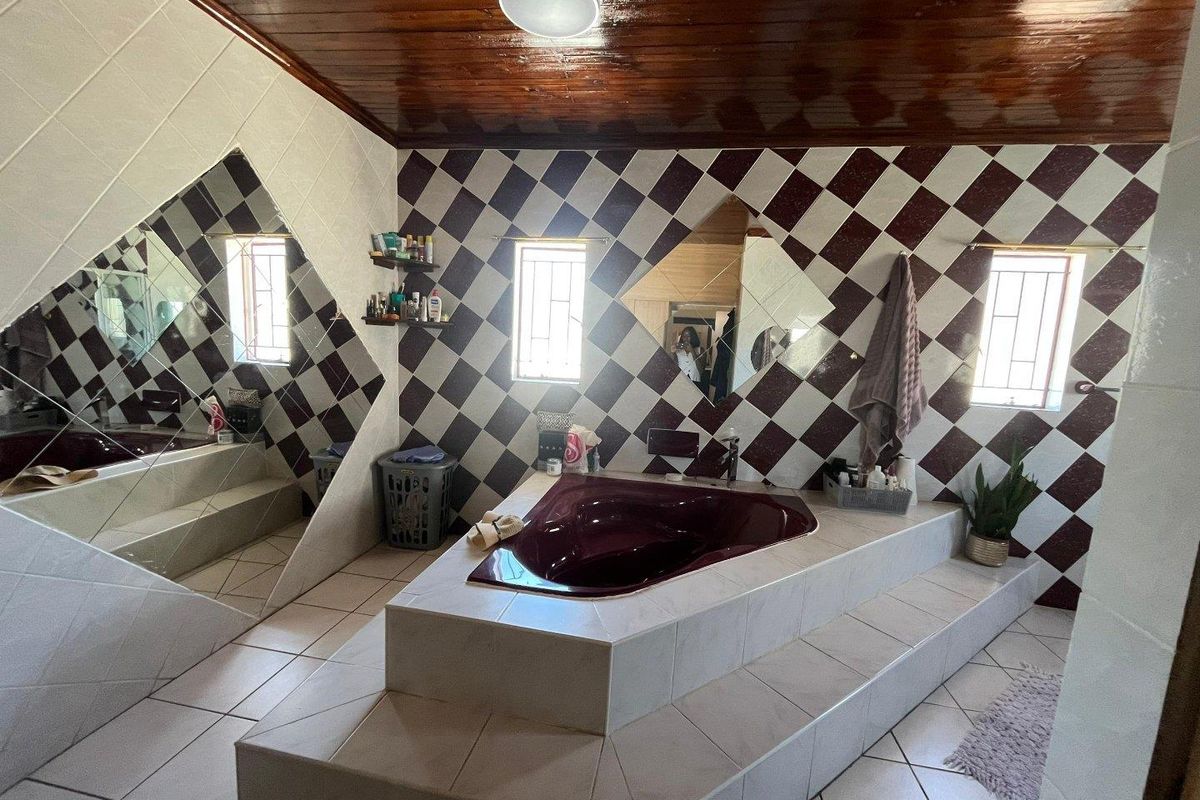 A spacious bathroom featuring a large corner bathtub, diamond-patterned wall tiles, and a timber-paneled ceiling with integrated lighting.