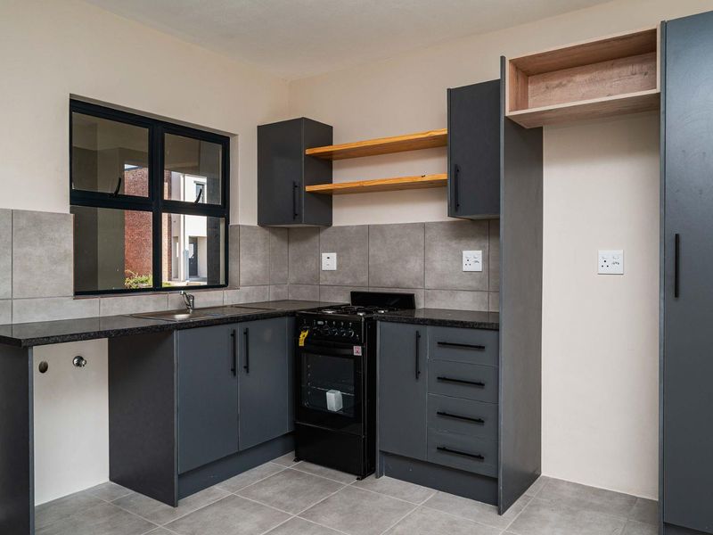 Modern kitchen featuring dark grey cabinetry, granite countertops, tiled backsplash, and a freestanding stove, offering a clean and functional workspace.