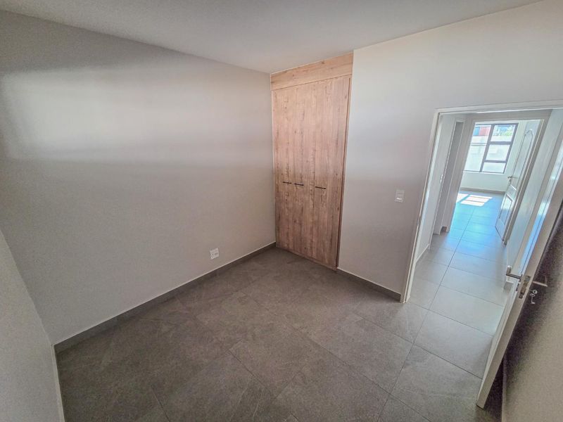 A clean, empty bedroom featuring modern wood-finish built-in wardrobes and neutral tiled flooring, offering a bright and versatile living space.