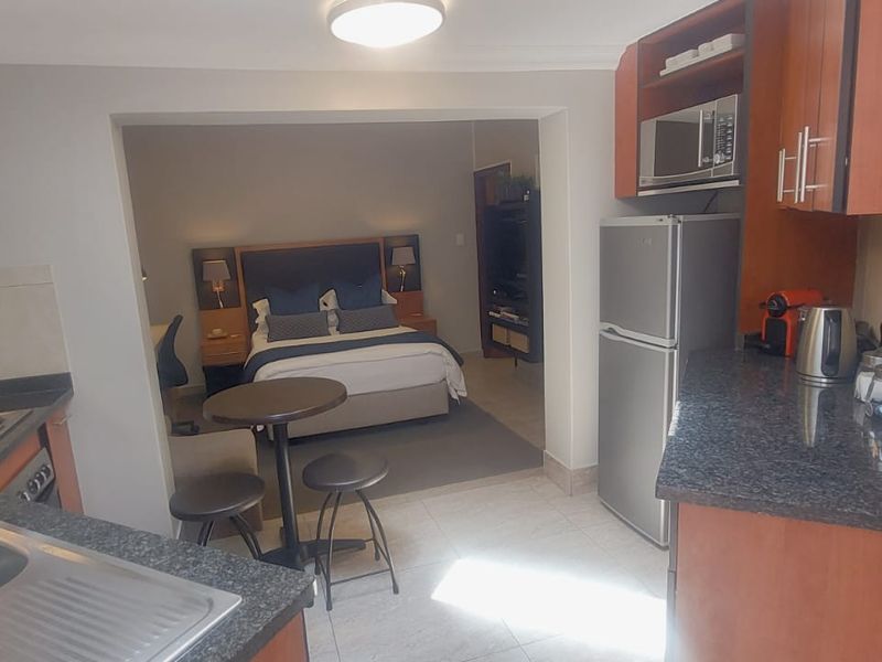 Open-plan kitchen and bedroom area featuring wooden cabinetry, granite countertops, and tiled flooring in a functional studio apartment layout.