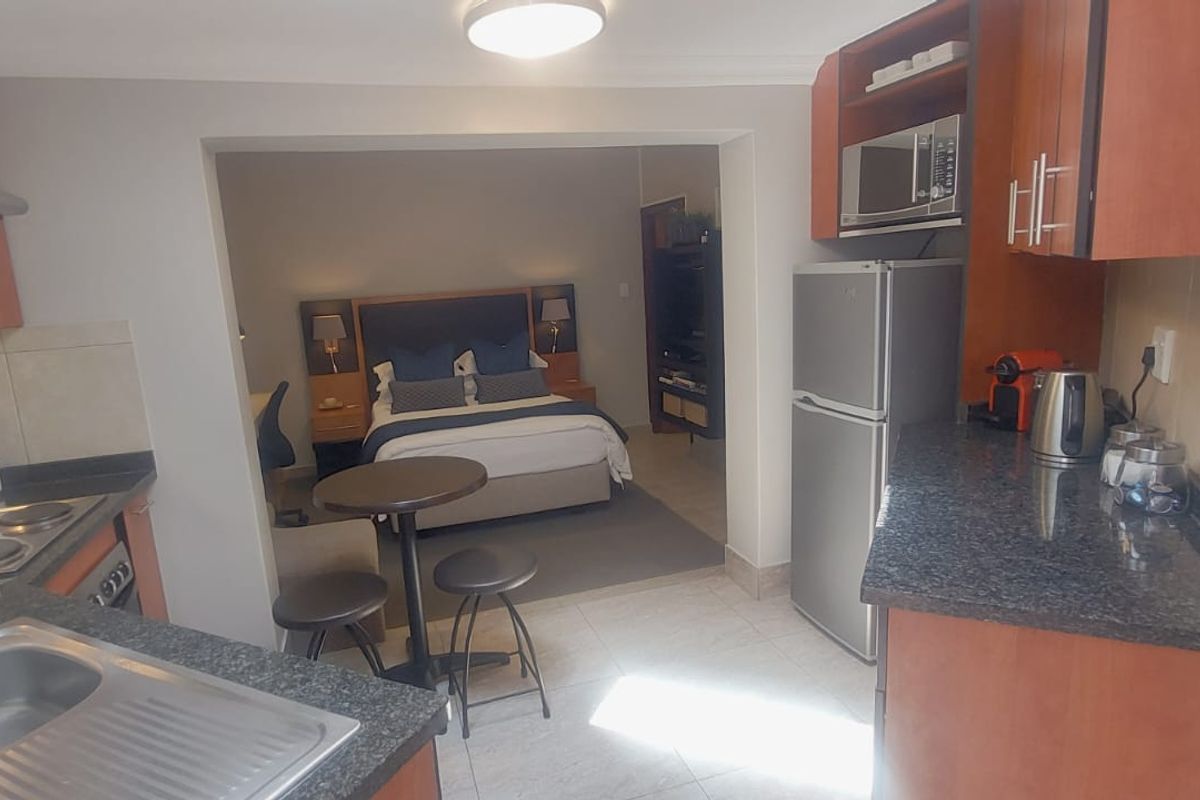 Open-plan kitchen and bedroom area featuring wooden cabinetry, granite countertops, and tiled flooring in a functional studio apartment layout.
