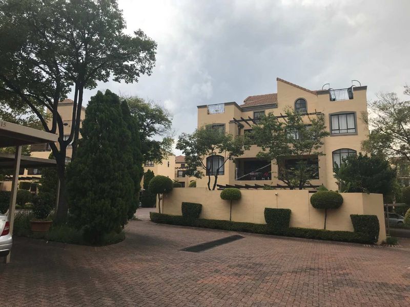 Exterior view of a multi-story apartment complex featuring paved driveway access, perimeter walling, and balconies with pergola structures.