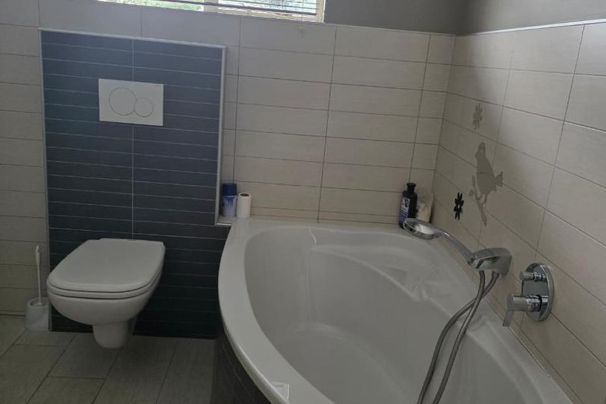 A modern bathroom featuring a wall-mounted toilet, a curved built-in bathtub with chrome fixtures, and neutral wall tiling with decorative accents.