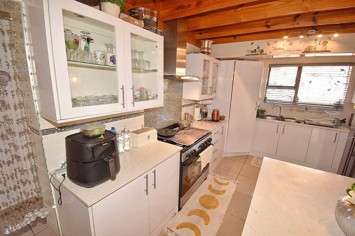 A well-lit kitchen featuring white cabinetry, stone countertops, a mosaic backsplash, and exposed timber ceiling beams, providing a warm and functional cooking space.