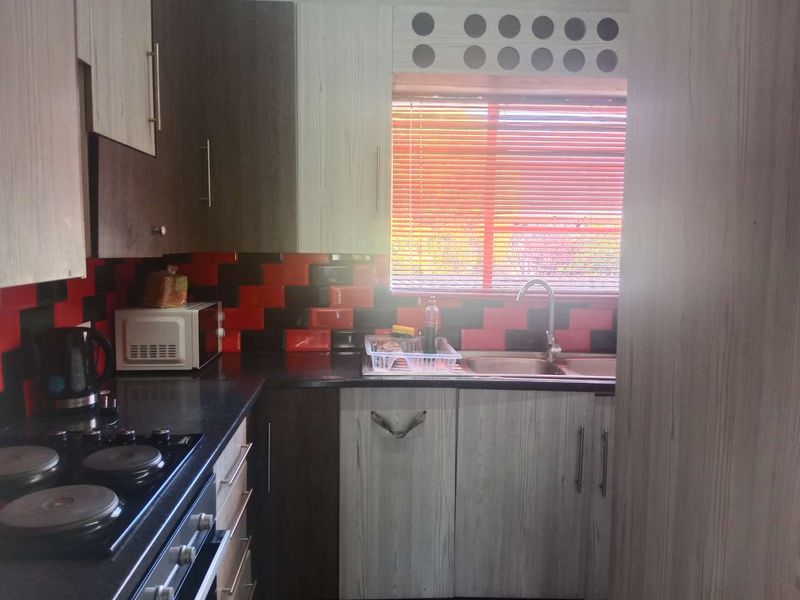 A functional kitchen featuring built-in cabinetry, laminate countertops, a double bowl sink, and a built-in electric hob and oven with a tiled splashback.