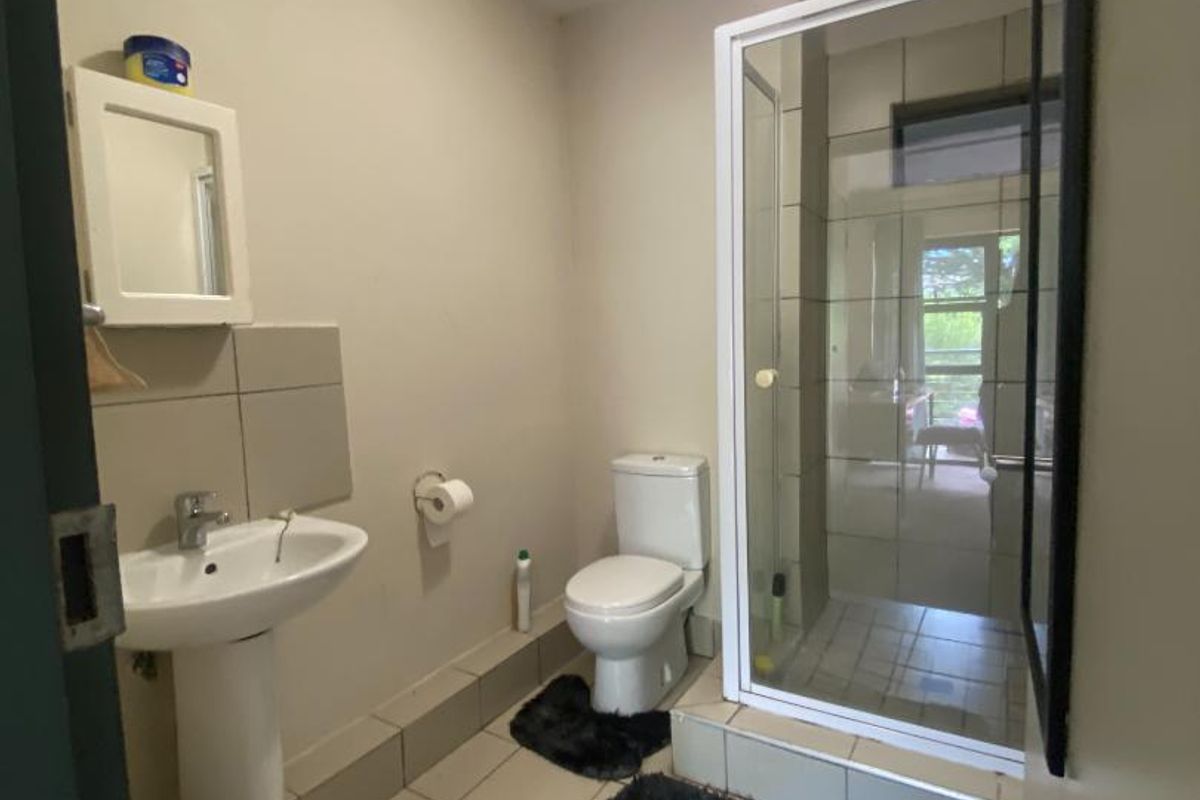 A functional bathroom featuring a pedestal basin, a toilet, and a glass-enclosed shower with tiled flooring.