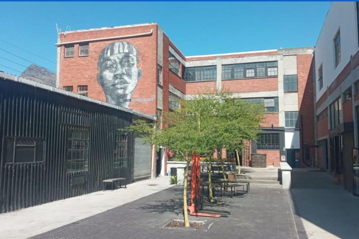 An industrial-style courtyard featuring exposed brick architecture, large steel-framed windows, and a prominent mural, creating a unique mixed-use outdoor space.