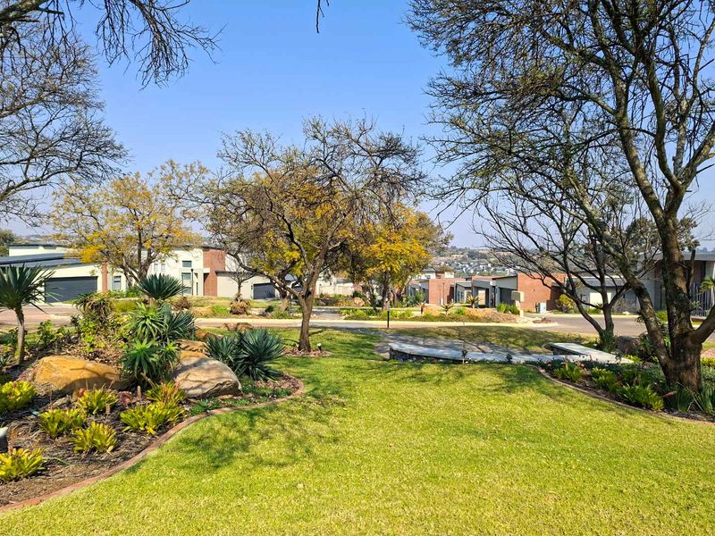 A well-maintained landscaped garden featuring mature trees, stone retaining walls, and paved pathways within a residential estate setting.
