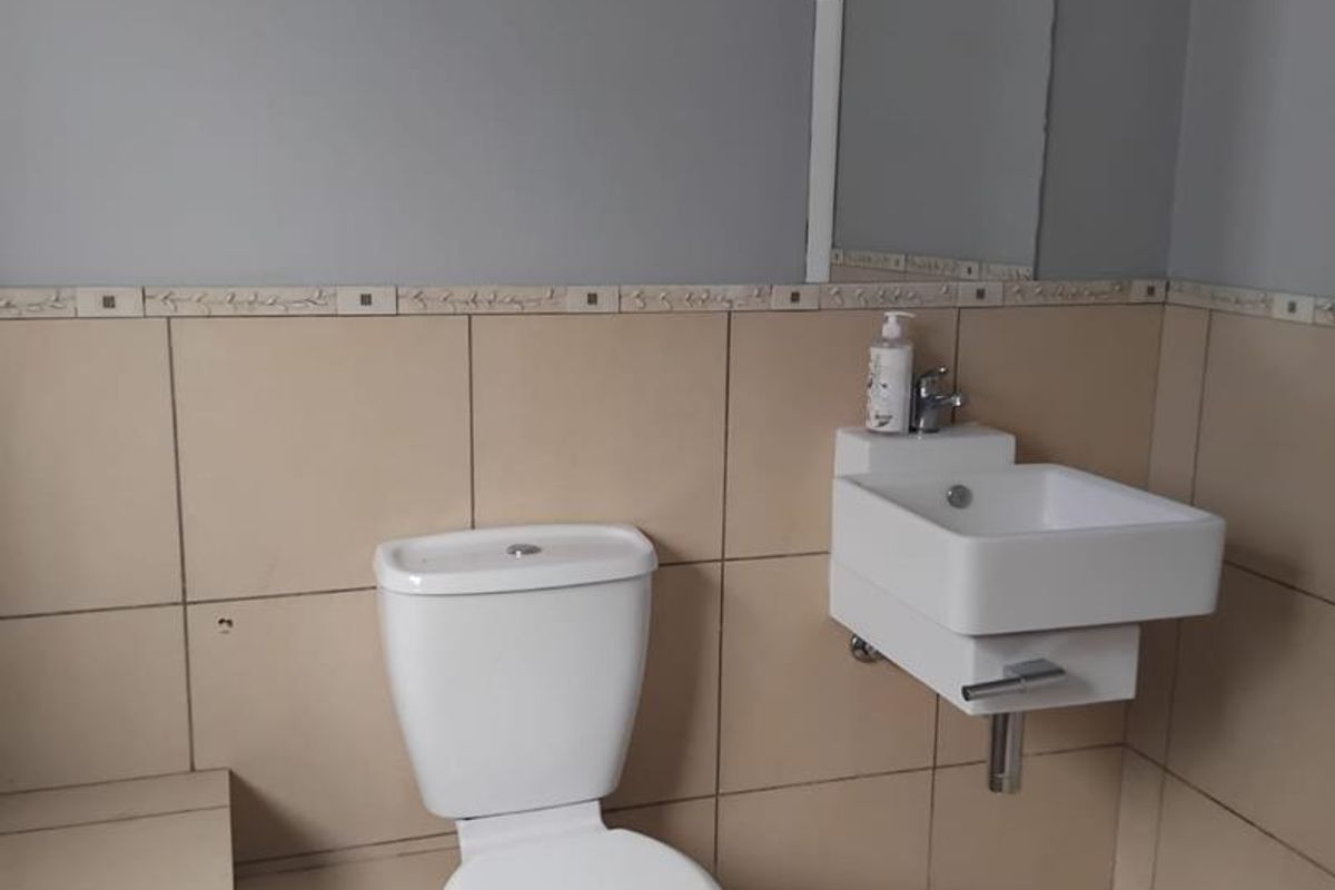A functional bathroom featuring a wall-mounted basin, a standard toilet, and neutral wall and floor tiling with a decorative border.