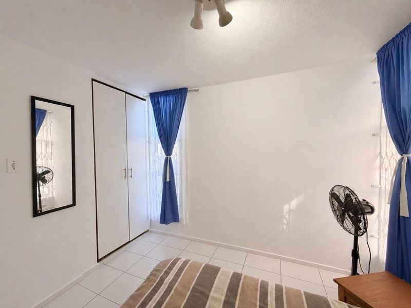 A bedroom featuring white tiled flooring, a built-in wardrobe, and windows fitted with security gates.