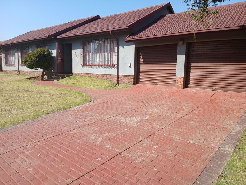 Front elevation of a single-story house featuring a paved driveway, double garage, and tiled roof with security bars on windows.