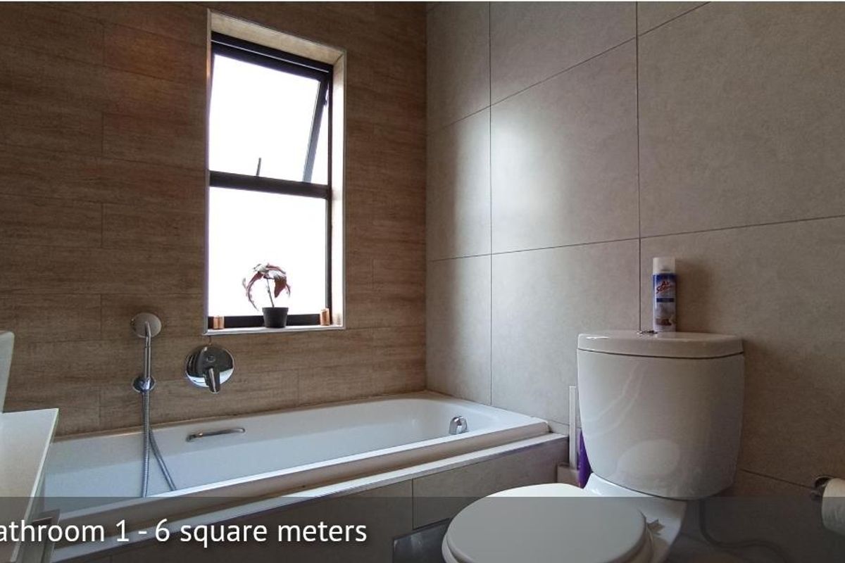 A modern bathroom featuring a built-in bathtub with wall-mounted mixer, a toilet, and neutral wall tiling.