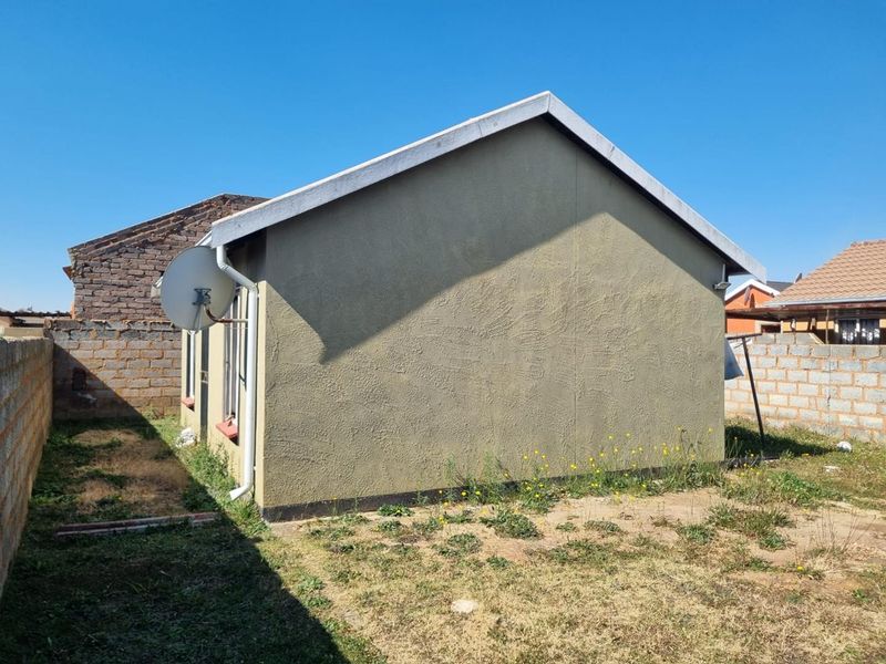 Rear view of the property showing the exterior wall, satellite dish, and surrounding yard area with boundary walls.