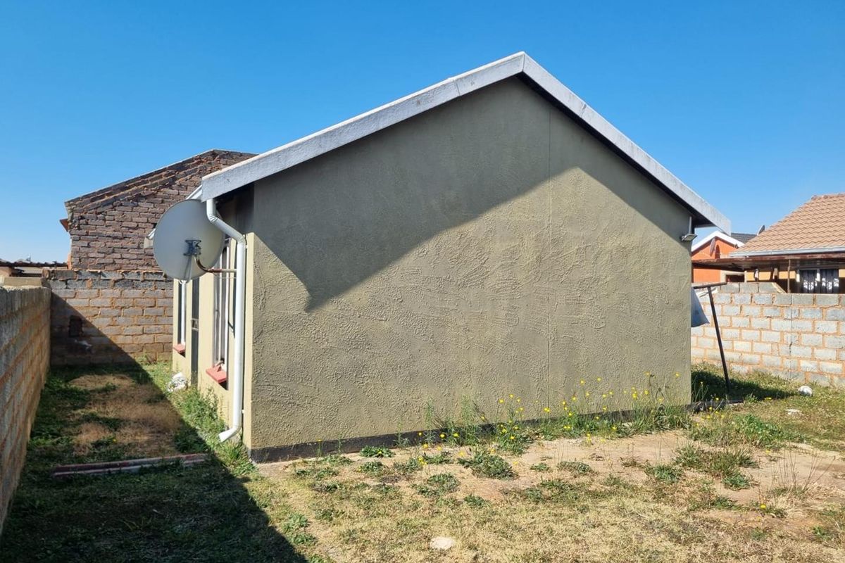 Rear view of the property showing the exterior wall, satellite dish, and surrounding yard area with boundary walls.