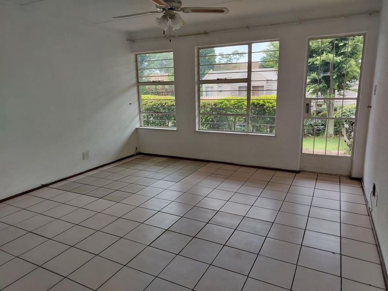 An empty living room featuring tiled flooring, a ceiling fan, and large windows providing natural light and access to the exterior.